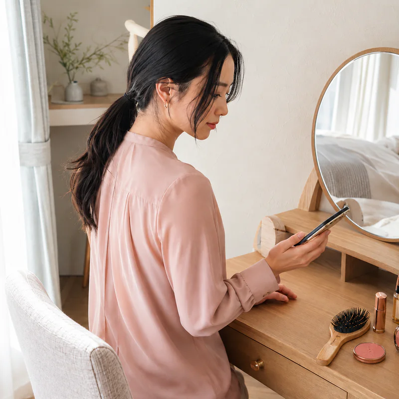 出勤前、鏡台の前でスマートフォンを見る成人女性のイメージ。